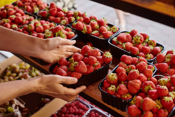 abgeschnittene Ansicht von reifen Verkäufer hält Packung mit frischen nahrhaften lebendigen Erdbeeren im Lebensmittelgeschäft - Foto, Bild