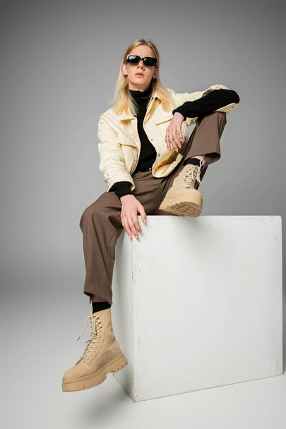 young attractive non binary model posing on white cube and looking at camera, fashion concept - Photo, Image