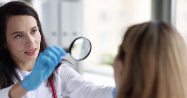 Дерматолог осматривает лицо пациента увеличительным стеклом. Концепция проблемы кожи - Кадры, видео