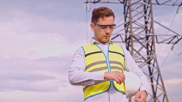 A designer inspects a high voltage tower. An engineer in a hard hat servicing a power transmission pylon. Electrical engineer in a power line wearing a helmet. A designer checks a high voltage sensor - Footage, Video