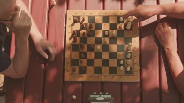 Draufsicht auf zwei erwachsene grauhaarige Männer, die an sonnigen Tagen am Tisch im Freien Schach spielen - Filmmaterial, Video