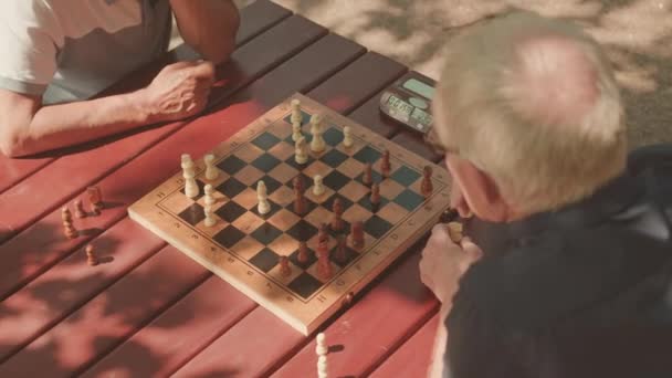 Υψηλής γωνίας βολή δύο ηλικιωμένων που παίζουν σκάκι στο τραπέζι σε εξωτερικούς χώρους - Πλάνα, βίντεο