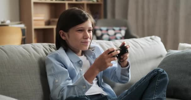 Victorious Caucasian schoolboy, holding a gamepad, celebrates a triumphant win in a video game while seated on the couch. His elation and gaming achievement create an atmosphere of success. - Footage, Video