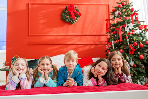 Καλά Χριστούγεννα και καλές γιορτές. Ομάδα παιδιών που διασκεδάζουν στο πιτζάμα πάρτι στο δωμάτιο των Χριστουγέννων. Άνετο σπίτι. - Φωτογραφία, εικόνα