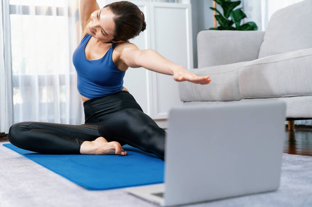 Computadora portátil enfocada en el suelo que muestra video de entrenamiento de ejercicio en línea, mientras que la mujer atlética deportiva se concentra en la rutina de calentamiento y estiramiento en un fondo borroso. Vigoroso - Foto, Imagen
