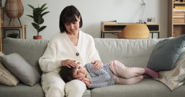 Nurturing mother communicates with preschool aged daughter on the couch. Their loving interaction reflects a moment of maternal care and valuable parent-child communication within the family. - Footage, Video