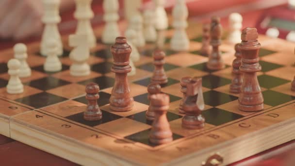 Nahaufnahme einer unkenntlichen männlichen Hand, die mit einer Schachfigur auf einem hölzernen Schachbrett Zug macht - Filmmaterial, Video