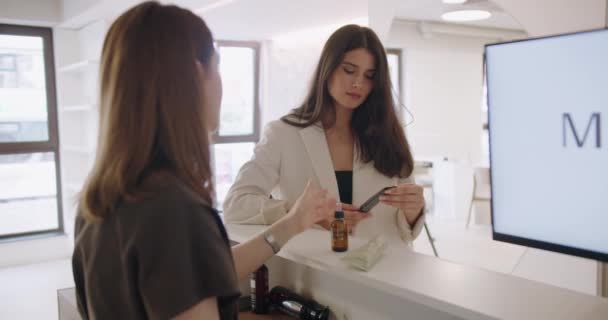 Kadın müşteri güzellik salonunda yüz bakımı için kremi seçiyor. Kadın danışman cilt bakımı için profesyonel kozmetik ürünleri öneriyor. - Video, Çekim