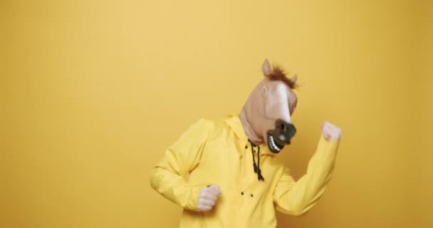 Άνθρωπος με μάσκα αλόγου κάνει αστείες χειρονομίες. Αστείος τύπος με κίτρινα κοστούμια Χορός με μάσκα αλόγου, ο άνθρωπος που διασκεδάζει σε απομονωμένο κίτρινο φόντο. Διασκεδάζουμε, διασκεδάζουμε. Η Ημέρα των Τρελών. Ιδέα για μασκαράτα. - Πλάνα, βίντεο