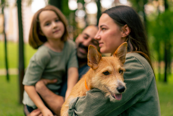 portret gelukkig jong gezin in park met hond vader houden dochter in armen concept vertrouwen zorg en familie waarden - Foto, afbeelding