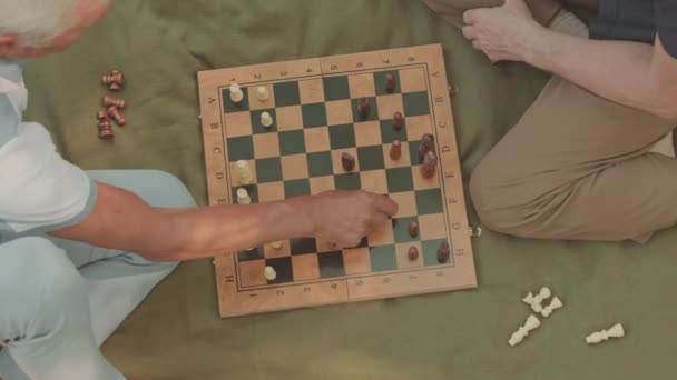 Draufsicht auf zwei unkenntlich gemachte männliche Freunde, die im Sommer auf grünen Plaids im Freien sitzen und in ihrer Freizeit Schach spielen - Filmmaterial, Video
