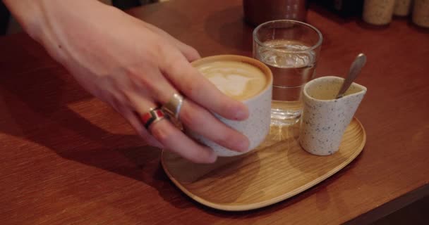 Vista cortada no barista preparou latte quente e mãos de servidor tomando xícara com bebida na bandeja de bambu para o cliente na cafeteria. Fechar de servir cappuccino em caneca de cerâmica no café - Filmagem, Vídeo
