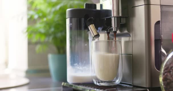 Máquina de café prepara e derrama café expresso em uma xícara de vidro com leite para preparar cappuccino ou latte. Imagens 4k de alta qualidade - Filmagem, Vídeo