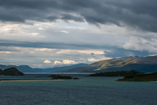 Piękna scena krajobrazowa Norwegii. Chmurna pogoda z górami częściowo rozjaśniona światłem słonecznym. Morze turkusowe. - Zdjęcie, obraz