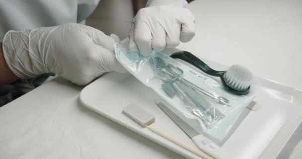 Closeup on master manicure hands in glove opening kraft package with clean sterile instruments for nails treatment procedures in beauty salon. - Footage, Video