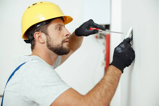 Portrait of male worker professional electrician in uniform installing electrical outlet in apartment after renovation work. Manual work, maintenance, occupation concept. Side view - Photo, image