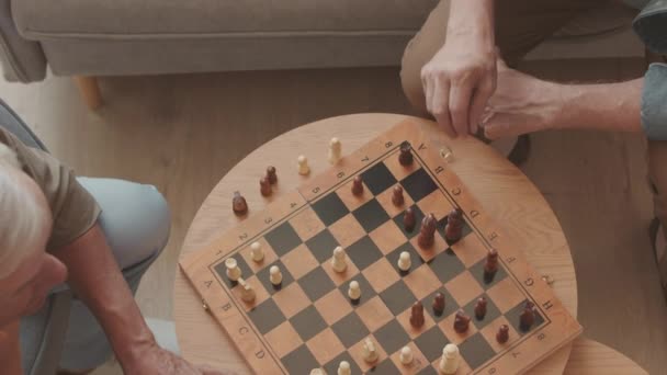 Top kilátás két ősz hajú érett férfi játszik sakk játék fa asztal beltéri - Felvétel, videó