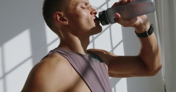 Sportieve man moe bij het sporten, het nemen van pauze en drinken van water uit de fles. Man bodybuilder rusten tussen lichaamsbeweging en vullen waterbalans - Video