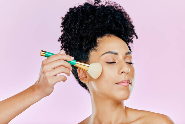 Face, makeup brush and a woman on a pink background in studio for facial cosmetology or skincare. Beauty, cosmetics and blush with a confident young model using tools to apply foundation to her skin. - Foto, immagini