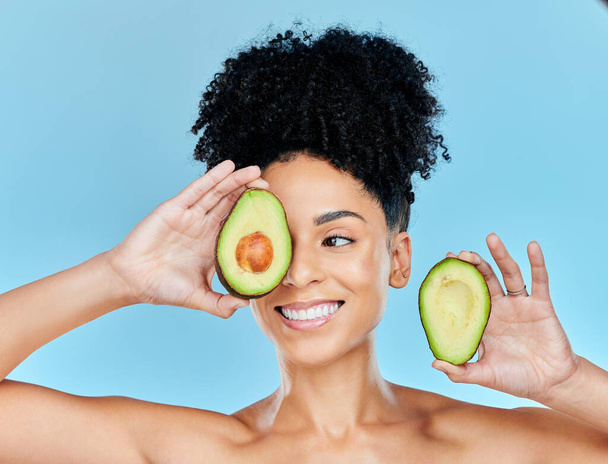Avocado, skincare and beauty, woman with natural benefits and product for face on blue background. Health, wellness and facial mask, smile with green fruit and vegan for dermatology in studio. - Photo, Image