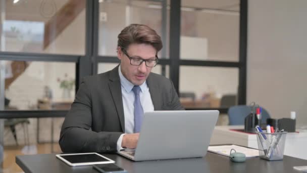 Liikemies Hymyilee kamerassa työskennellessään kannettavan tietokoneen toimistossa - Materiaali, video