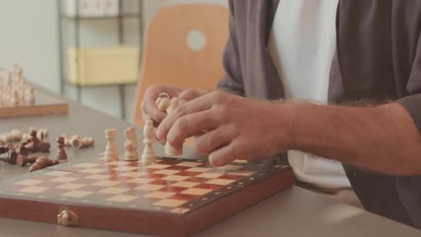 Обрізаний знімок невпізнаваного шахіста-чоловіка, який кладе фігури на дерев'яну дошку, готуючись до виклику - Кадри, відео