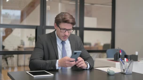 Geschäftsmann schockiert über Verlust am Telefon, während er im Büro auf einer Bank sitzt - Filmmaterial, Video