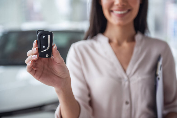 Besuch beim Autohaus. schöne junge Frau zeigt Schlüssel ihres neuen Autos, blickt in die Kamera und lächelt - Foto, Bild