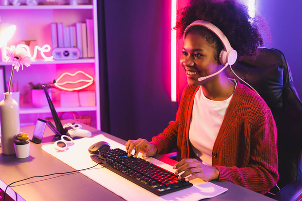 Gaming Streamer, afrikanisches Mädchen beim Online-Kampf mit dem Esport-Team, das Kopfhörer in neonfarbener Beleuchtung trägt. Gespräche mit anderen Spielern, die Strategien planen, um Konkurrenten zu gewinnen. Geschmacksmacher. - Foto, Bild