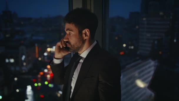 Displeased entrepreneur talking phone late evening at office window closeup. Angry businessman shouting at telephone conversation feeling stress. Annoyed bearded manager arguing with partners at night - Footage, Video