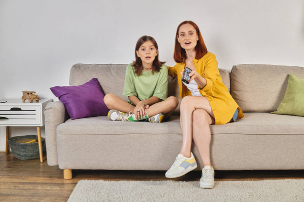 zdumiona kobieta z nastoletnią córką oglądającą film na przytulnej kanapie w nowoczesnym salonie, wypoczynek - Zdjęcie, obraz