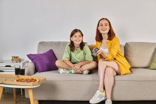 mãe feliz e filha adolescente assistindo tv no sofá perto de pizza e óculos com refrigerante na sala de estar - Foto, Imagem