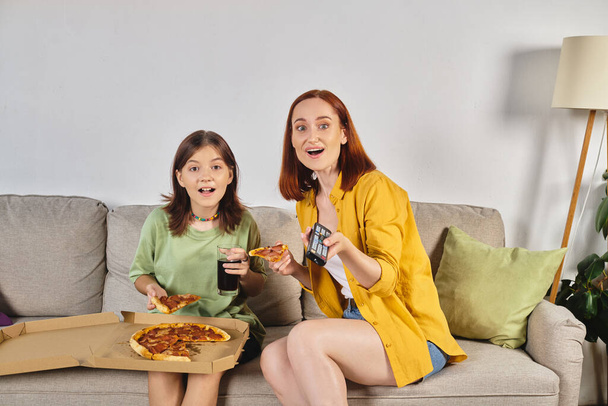リビングルームでピザとソーダと一緒に座っている間,テレビを見ている驚いた母親とティーン娘 - 写真・画像