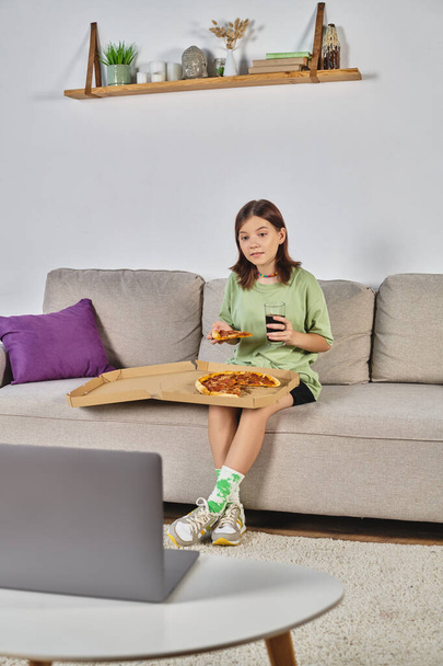 έφηβος κορίτσι κάθεται στον καναπέ με πίτσα και σόδα και βλέποντας ταινία στο laptop, αναψυχή στο σπίτι - Φωτογραφία, εικόνα