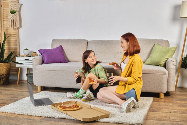 happy mother and teen daughter with pizza and soda watching movie on laptop on floor in living room - Photo, Image