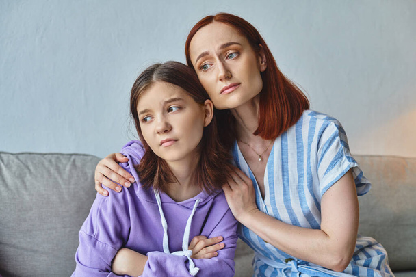 worried mother embracing and calming upset teenage daughter at home in living room, support and care - Фото, зображення