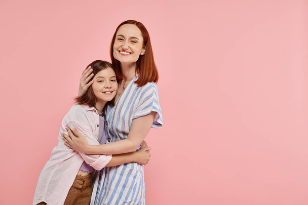 ευτυχισμένη γυναίκα με έφηβη κόρη σε κομψό casual ενδυμασία κοιτάζοντας κάμερα σε ροζ φόντο - Φωτογραφία, εικόνα