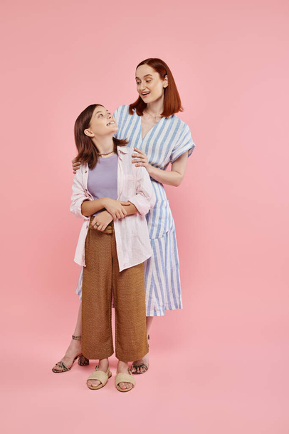 full length of happy and stylish mother with teenage daughter looking at each other on pink - Photo, Image