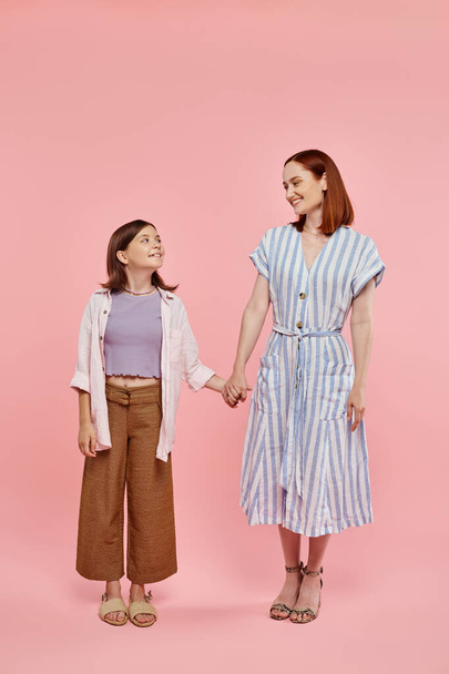 pełna długość wesołej kobiety z nastolatką trzymającą się za ręce i uśmiechającą się do siebie na różowo - Zdjęcie, obraz