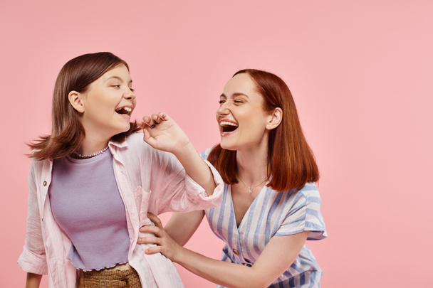 excited stylish woman with cheerful teenage daughter having fun and laughing on pink backdrop - Photo, Image