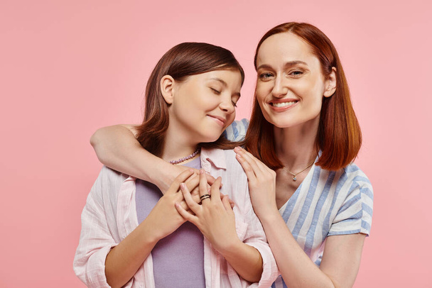 opgewonden en geïnspireerd vrouw omarmen tiener meisje op roze achtergrond, eenheid van moeder en dochter - Foto, afbeelding