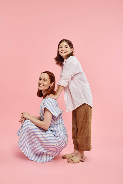 veselý stylový žena sedící na patách v blízkosti dospívající dcera pózovat na růžovém pozadí, zábava a radost - Fotografie, Obrázek