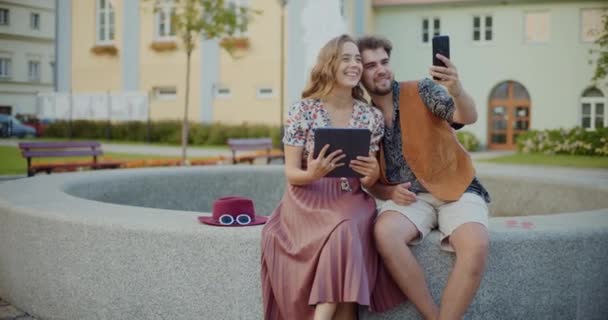 Adam akıllı telefondan selfie çekiyor ve elinde dijital tablet tutan bir kadın arkadaşı var. - Video, Çekim