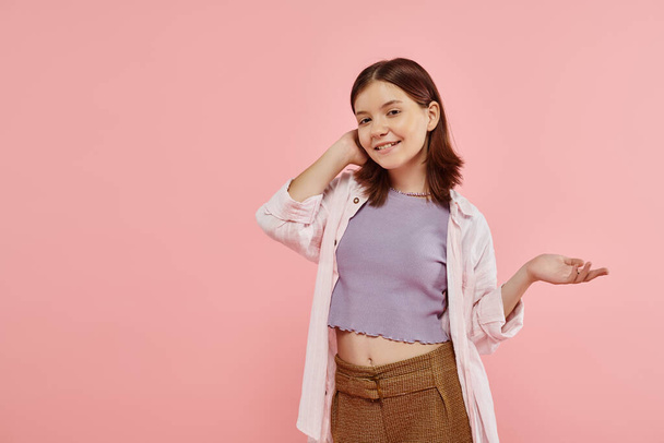 radostné dospívající dívka ve stylové ležérní oblečení ukazuje rukou a dívá se na kameru na růžové - Fotografie, Obrázek