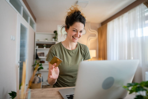 Jedna žena dospělý kavkazský žena sedět doma šťastný úsměv na notebooku držet bankovní kreditní karty on-line nákupní koncept skuteční lidé kopírovat prostor e-commerce - Fotografie, Obrázek