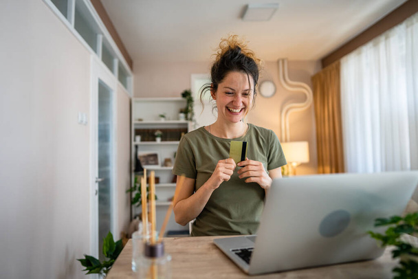 One woman adult caucasian female sit at home happy smile at laptop computer hold bank credit card online shopping concept real people copy space e-commerce - Photo, Image