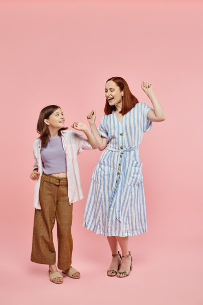 full length of carefree and trendy woman with preteen daughter dancing on pink backdrop in studio - Photo, Image