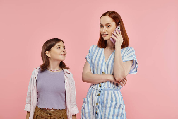 trendige Frau, die auf dem Handy neben lächelndem preteen girl auf rosa Hintergrund, moderne Mutter und Teenager spricht - Foto, Bild