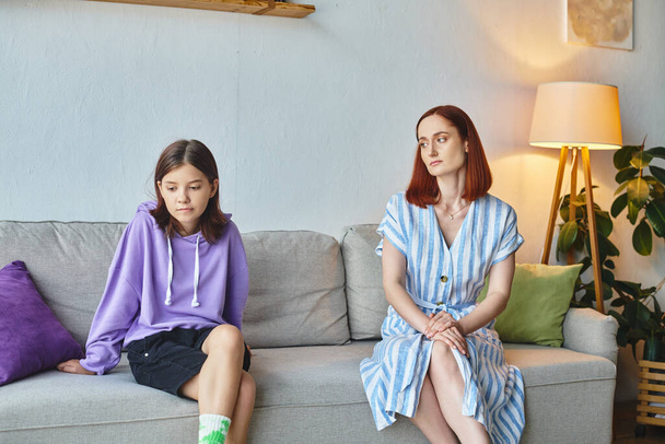 frustrated woman and offended preteen daughter sitting on couch in living room, generation gap - Foto, Imagen