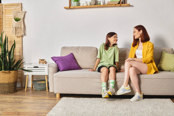 joyful mother and teenage daughter talking about sex education on couch in living room at home - Photo, Image